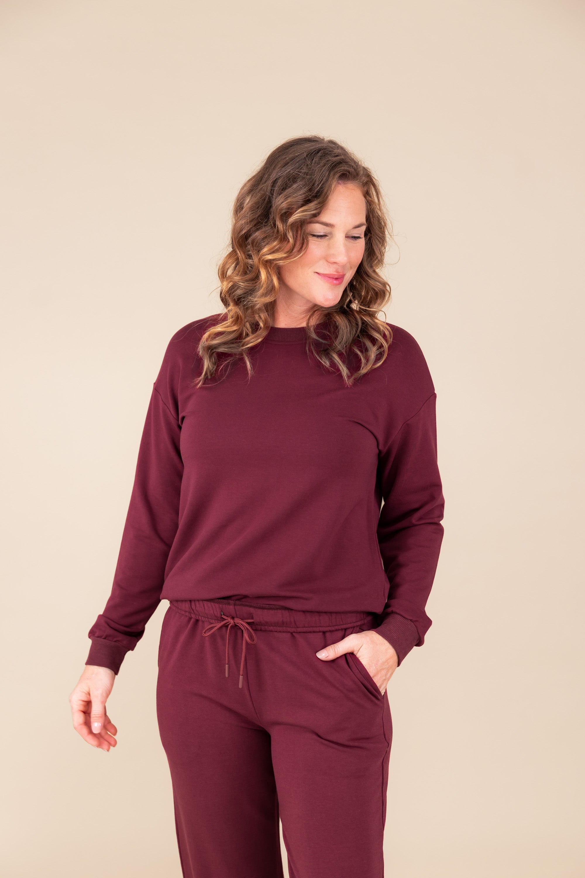 Woman wearing Women's Sweatshirt in Burgundy color over women's jogger pants in burgundy on a beige background ::: Model is 5'9" wearing size M ///