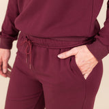 Modal wearing Women's Jogger Pant in Burgundy color with pockets under similar color sweatshirt on a beige background