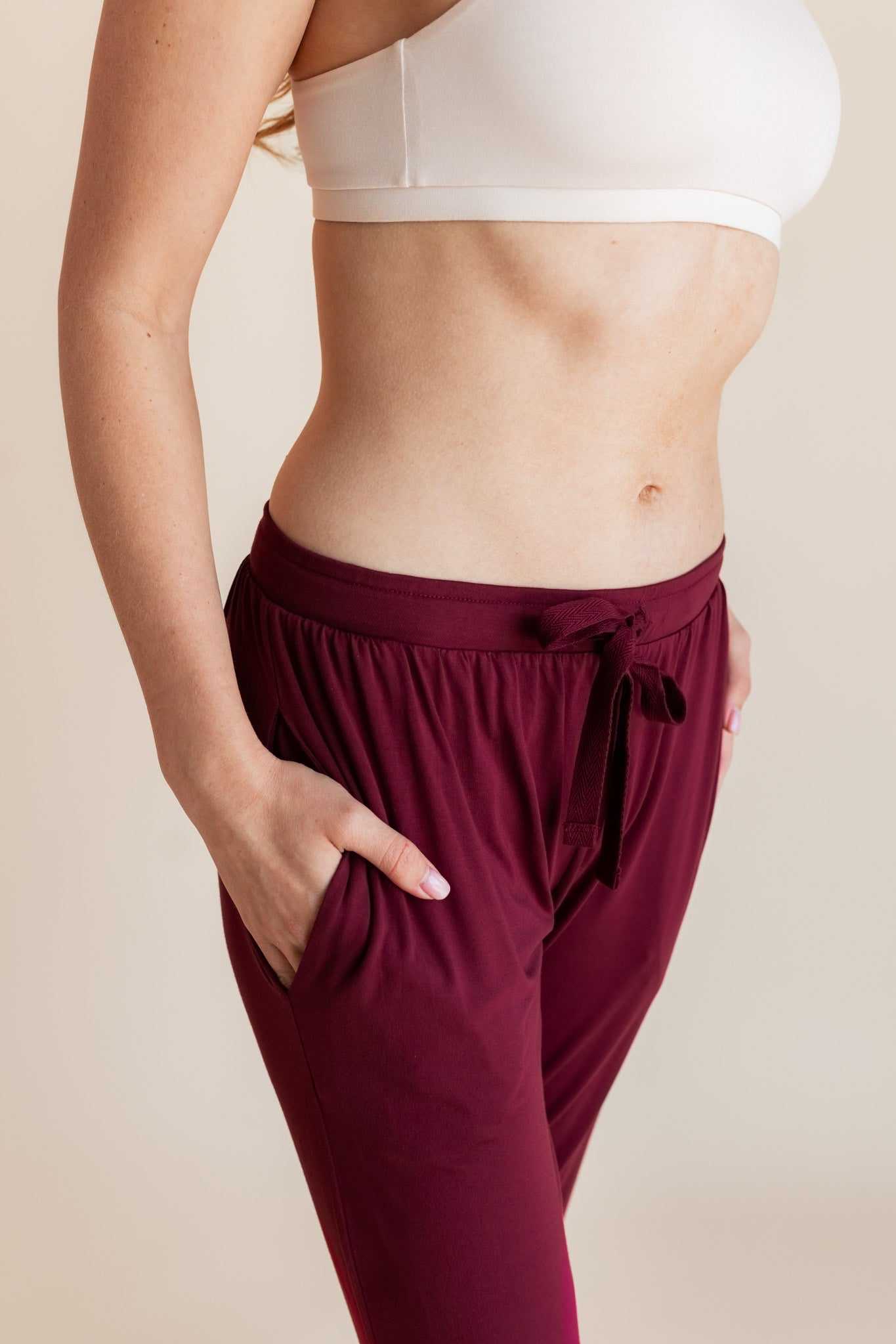 Model wearing burgundy jogger pant with drawstring waist and neutral bralette, showing pocket