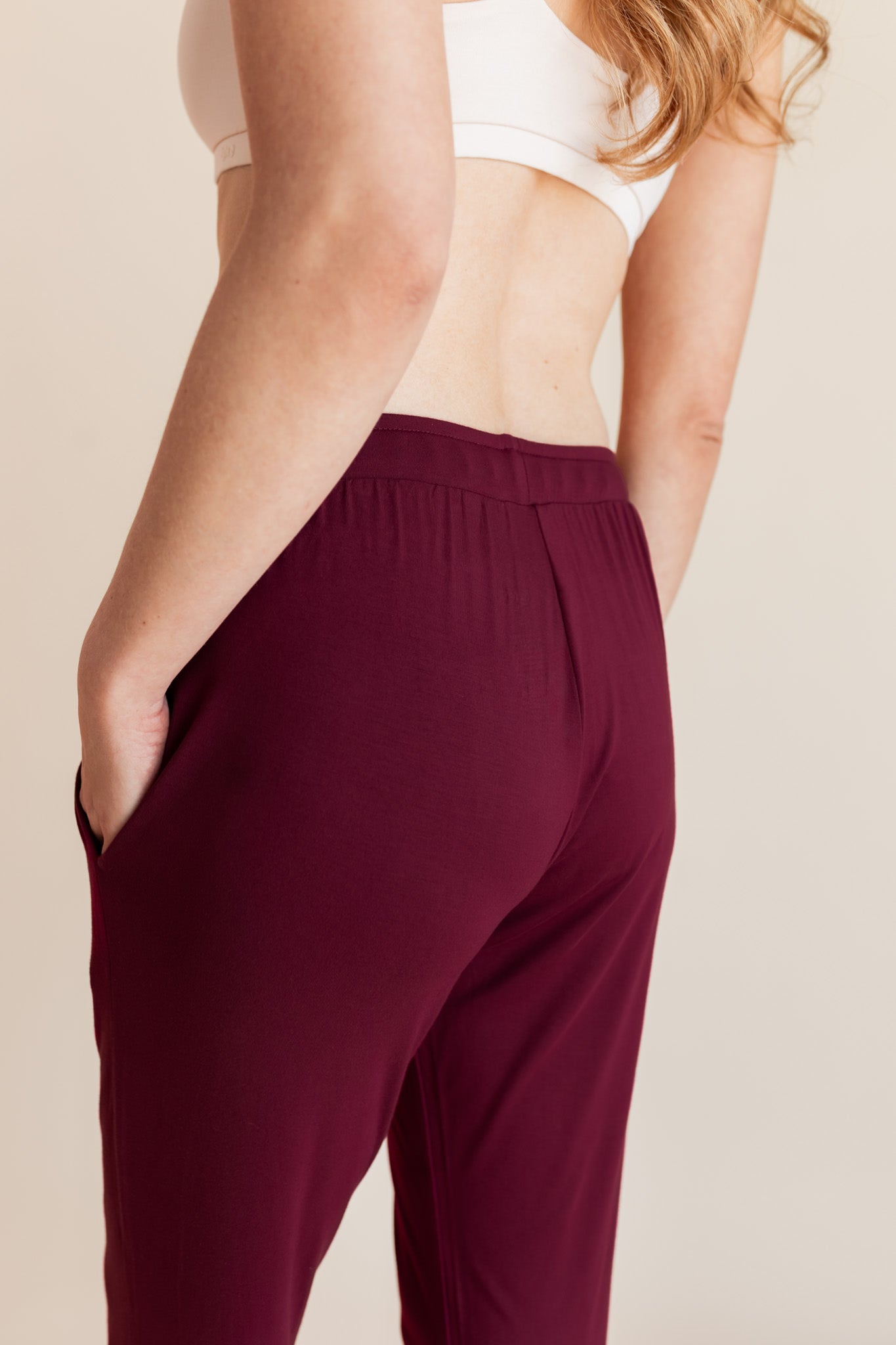 Model wearing burgundy jogger pant with drawstring waist and neutral bralette, showing back of pant