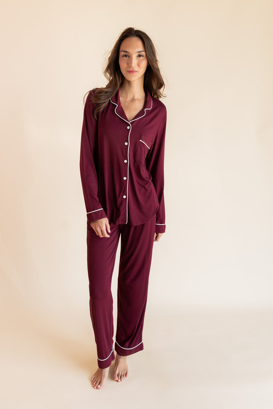 Woman modeling burgundy long sleeve pajama set with white piping in a studio setting