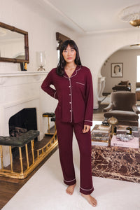 Woman wearing long sleeve burgundy pajama set with white piping in a luxury living room