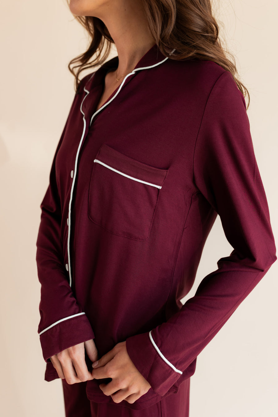 Woman modeling burgundy long sleeve pajama set with white piping, showing pocket detailing on top