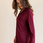 A woman wearing a long-sleeve burgundy button-up shirt dress, photographed against a solid light beige background.