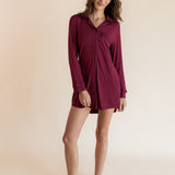 A woman modeling a long-sleeve burgundy button-up shirt dress against a solid beige studio background.