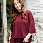 Model standing outside in front of a white brick wall while wearing the Women's Short Sleeve Tee in Burgundy