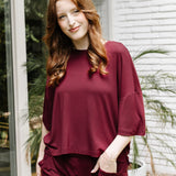 Model standing outside in front of a white brick wall while wearing the Women's Short Sleeve Tee in Burgundy