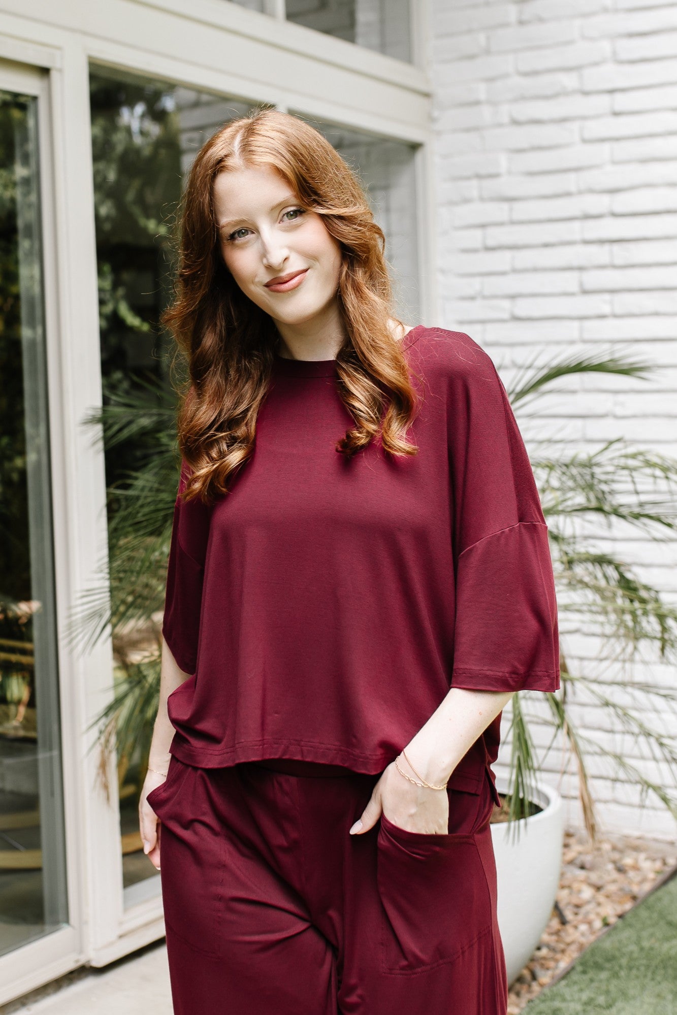 Model standing outside in front of a white brick wall while wearing the Women's Short Sleeve Tee in Burgundy