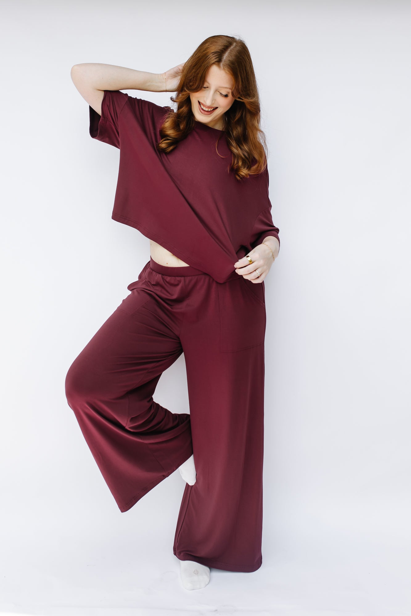 Model with hand in hair while wearing the Women's Short Sleeve Tee in Burgundy paired with matching wide leg pants