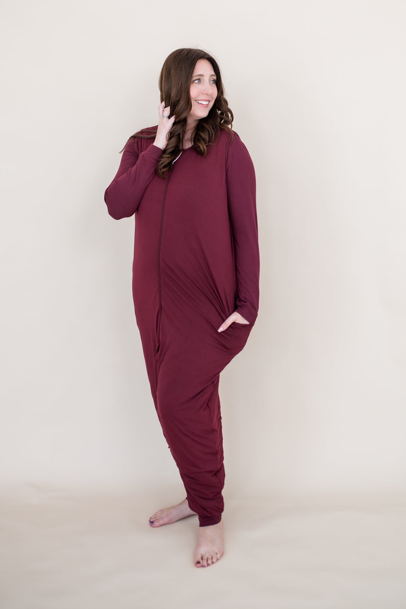 Smiling woman looking to the side while modeling the Kyte Adult Sleep Bag Walker in Burgundy with matching top beneath it