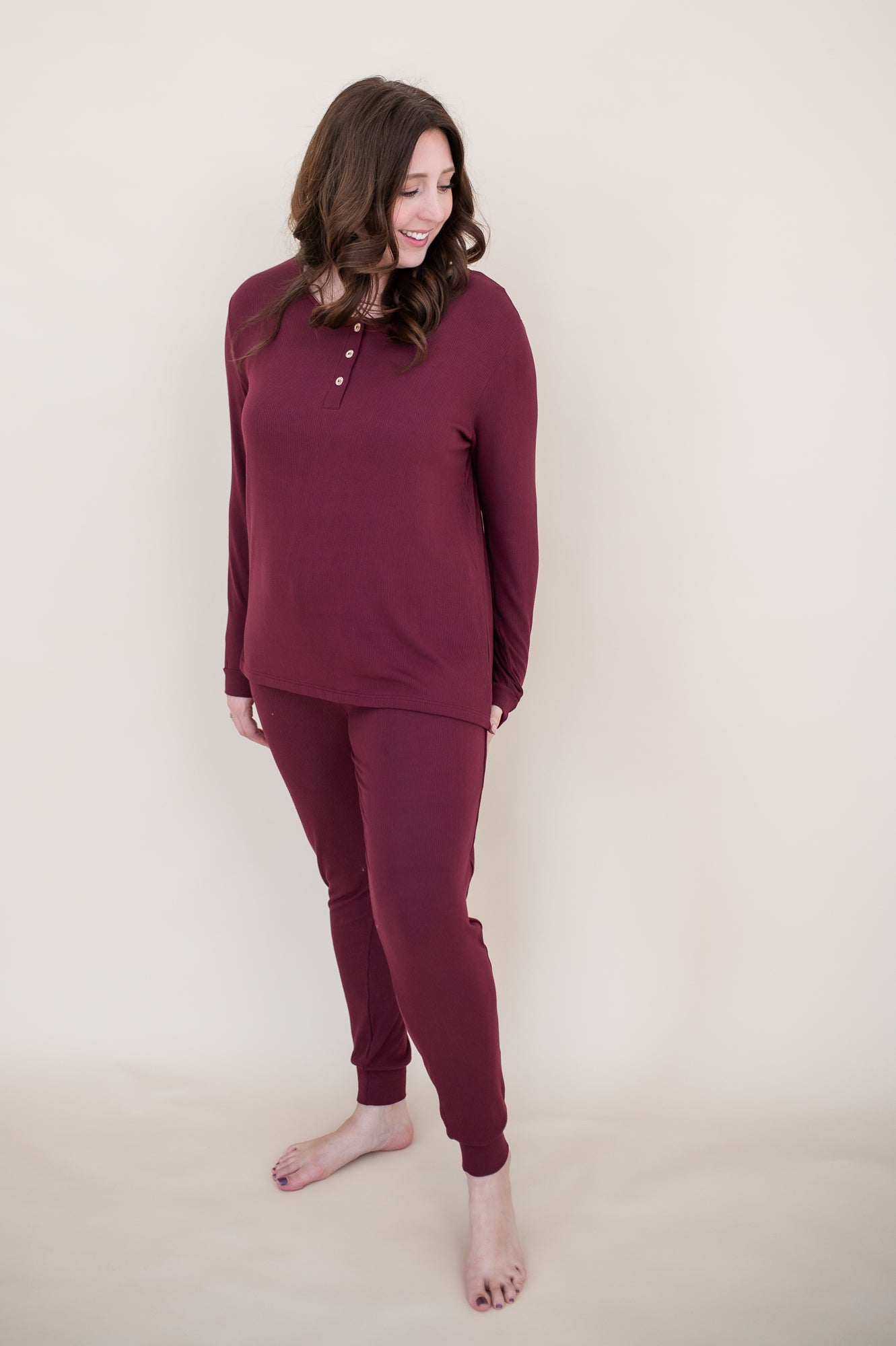 Woman looking downwards and smiling while modeling the Kyte  Long Sleeve Henley top in Burgundy 