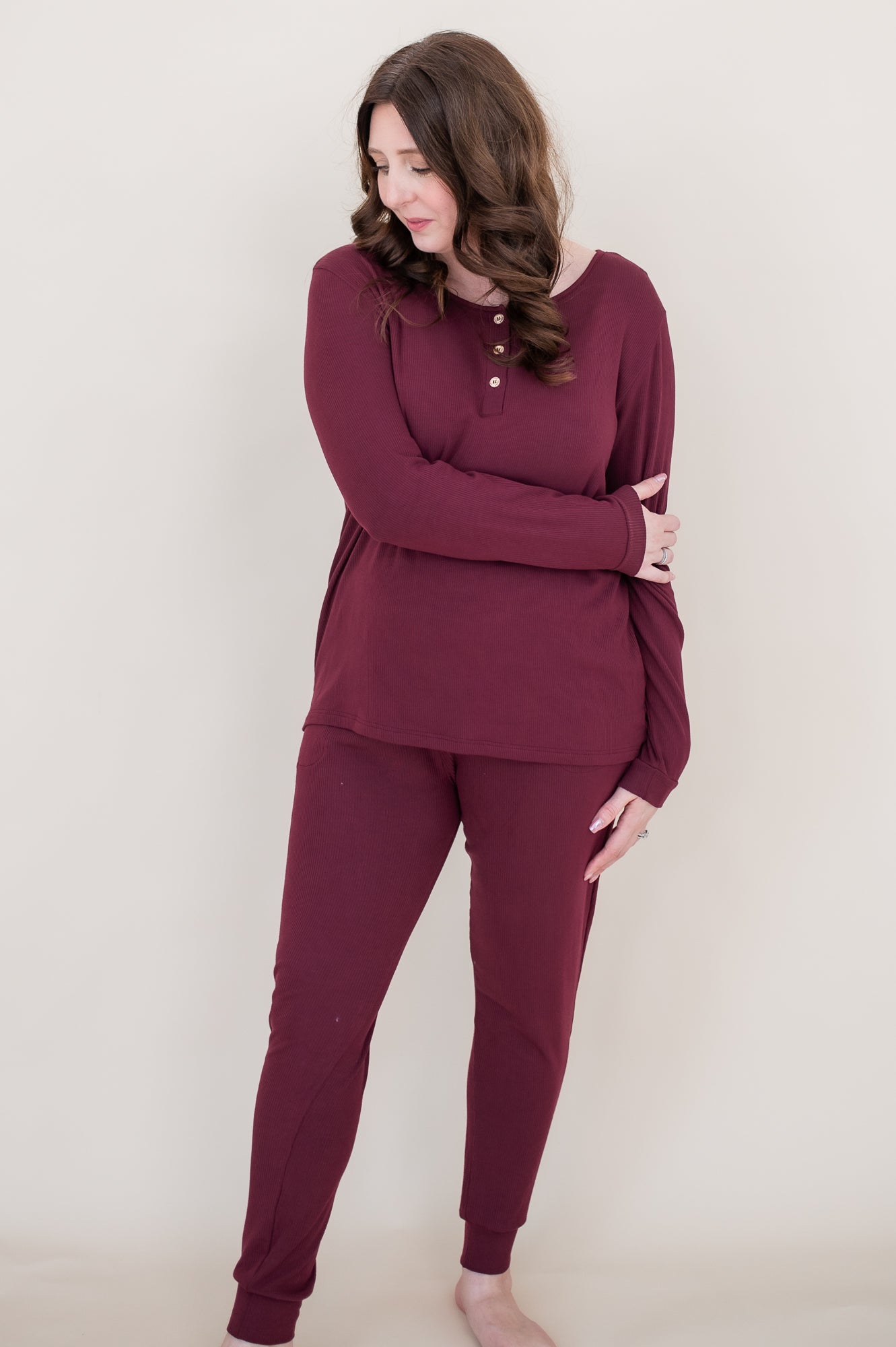 Woman looking downwards while modeling the  Women's Henley top in Burgundy paired with matching joggers