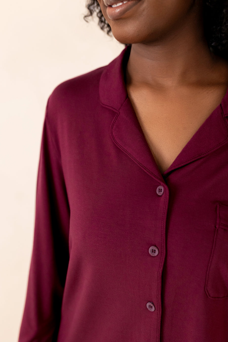 Close-up of a person wearing a burgundy shirt against a neutral background