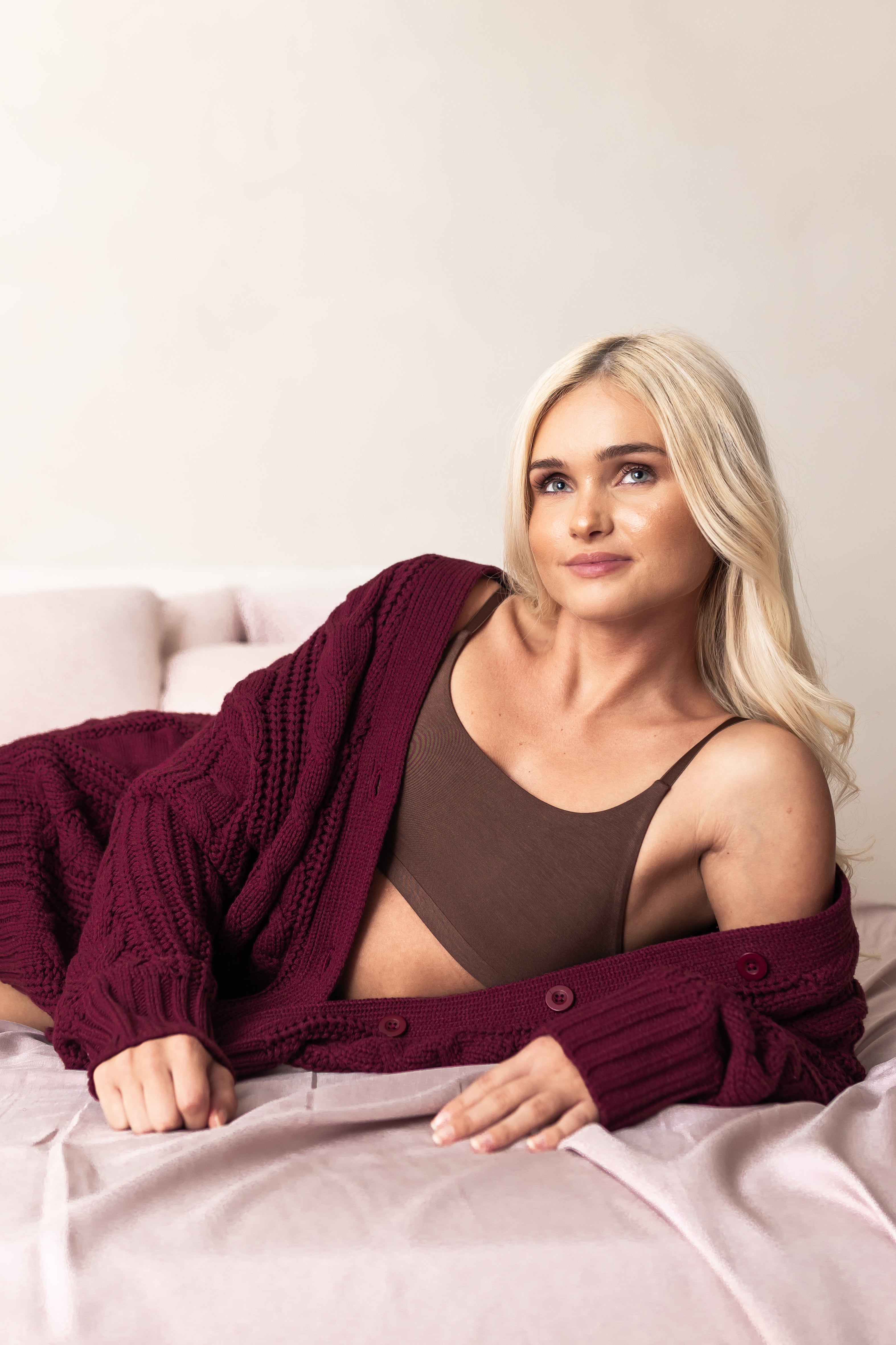Woman wearing a burgundy cardigan over a brown bralette on a light-colored background