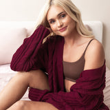 Woman wearing a burgundy cable knit bamboo cardigan and deep brown bralette sitting on a bed