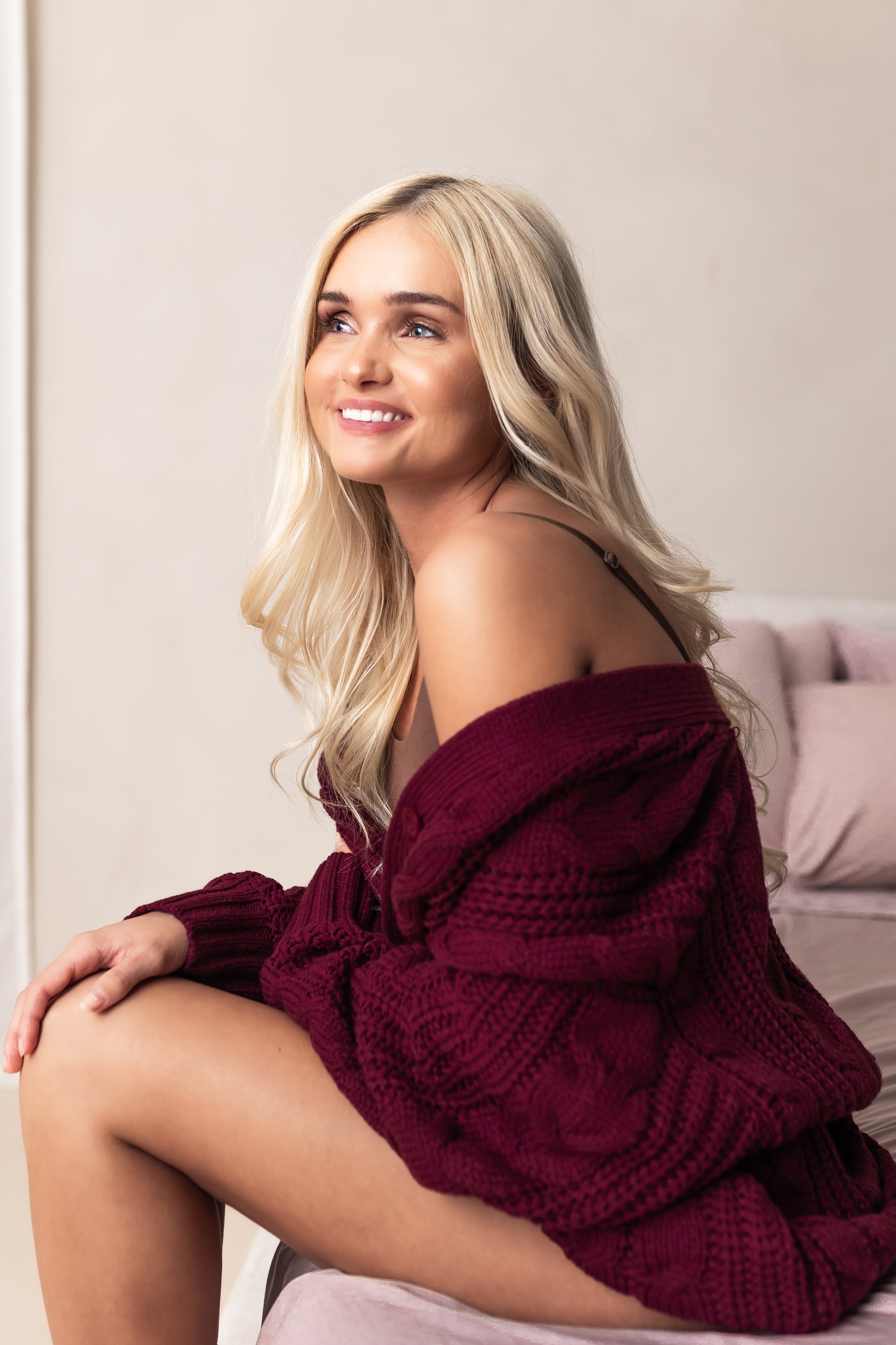 Woman wearing a burgundy knitted sweater sitting on a bed.