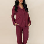 Model standing in front of a beige wall while wearing the Bamboo Long-Sleeved Women's Pajama Set in Burgundy with Burgundy Trim