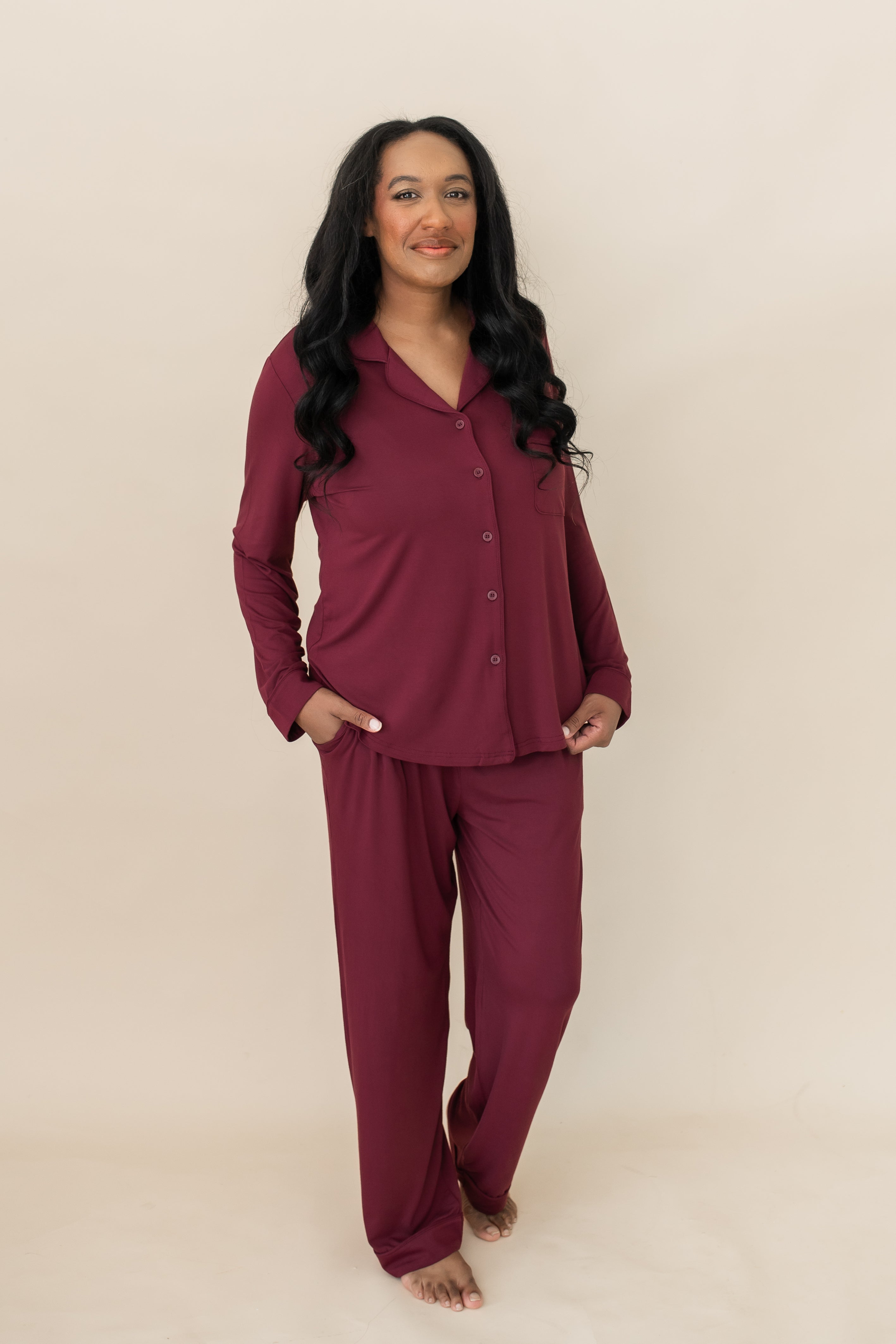 Model standing in front of a beige wall while wearing the Bamboo Long-Sleeved Women's Pajama Set in Burgundy with Burgundy Trim