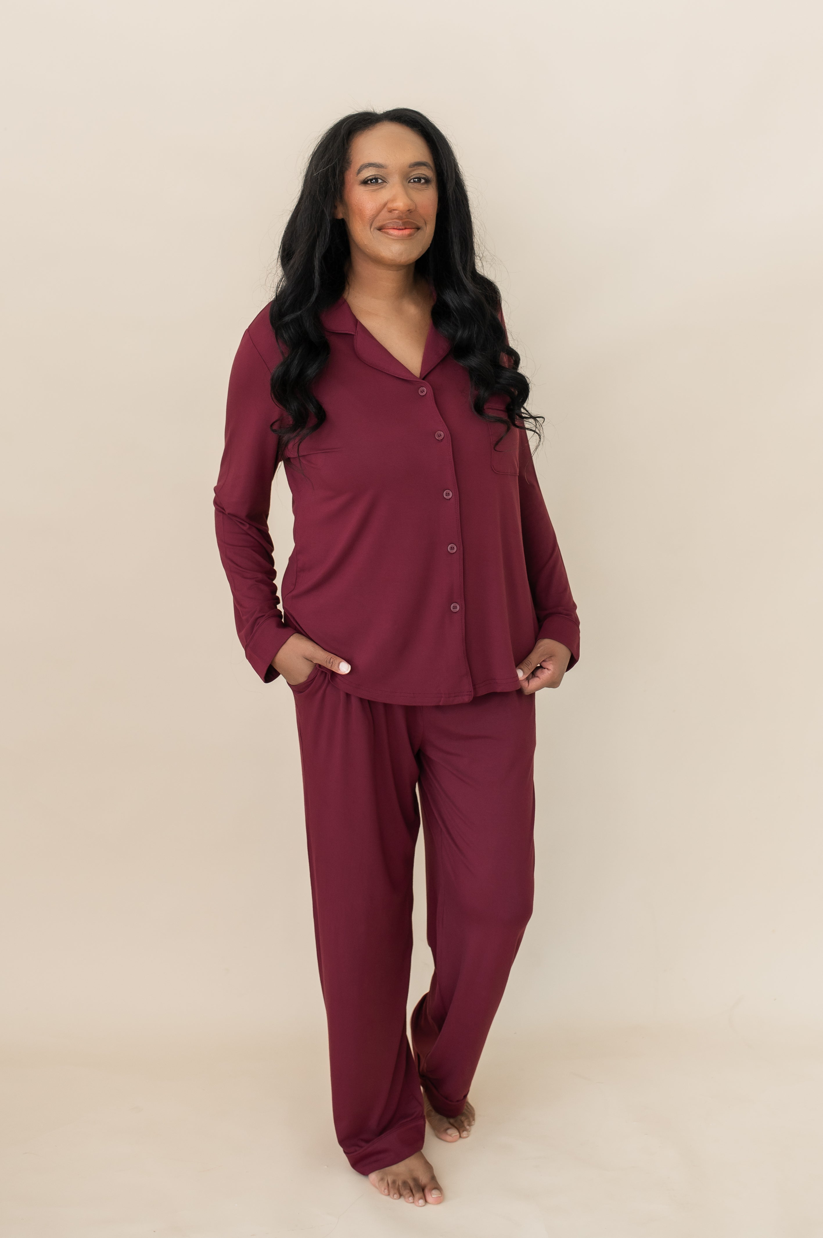 Model standing in front of a beige wall while wearing the Bamboo Long-Sleeved Women's Pajama Set in Burgundy with Burgundy Trim