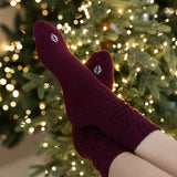 Burgundy socks with a logo worn by a person in front of a decorated Christmas tree.