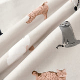 A close-up of draped fabric featuring a playful print of various cartoon-style cats in shades of gray, white, and warm tan on an off-white background.