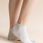 A close-up of a person's feet wearing light gray ankle socks against a solid beige background.