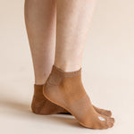 A close-up of a person's feet wearing tan low-cut athletic socks against a solid light beige background.