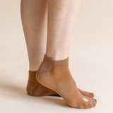 A close-up of a person's feet wearing tan low-cut athletic socks against a solid light beige background.