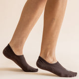 A close-up of a person's feet wearing dark brown low-cut no-show socks against a solid light beige background.