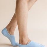 A close-up of a person's legs wearing light blue low-cut no-show socks against a solid beige background.