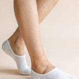 White low-cut no-show socks worn on a person's feet, shown against a solid light beige background.