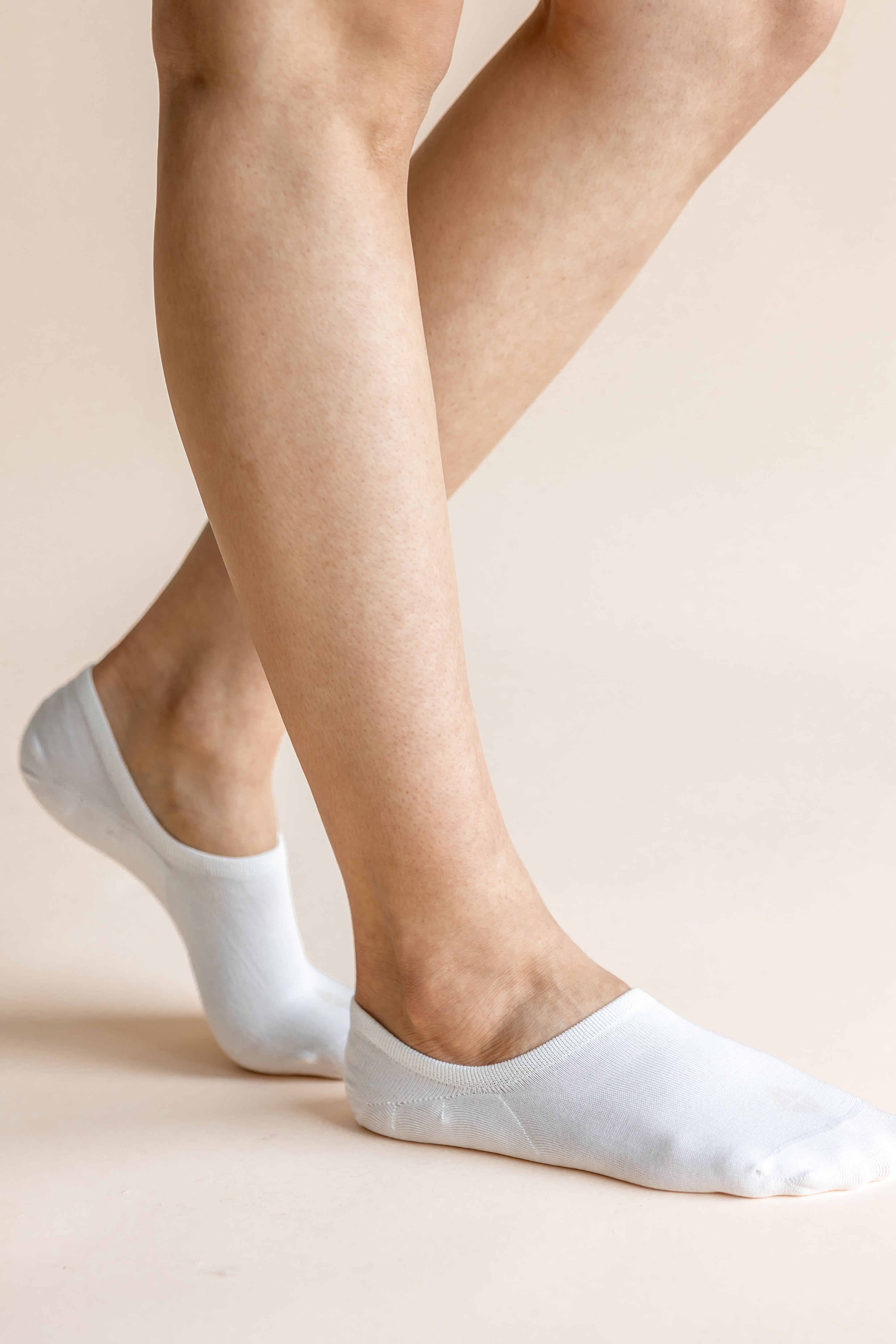 White low-cut no-show socks worn on a person's feet, shown against a solid light beige background.