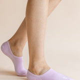 A close-up of a person's feet wearing light lavender low-cut no-show socks against a solid pale beige background.