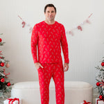 Male model standing in front of a cream ottoman between two decorated Christmas trees wearing the Men's Jogger Set in Candy Cane with one hand in the jogger pants pocket