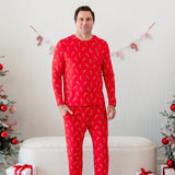 Male model standing in front of a cream ottoman between two decorated Christmas trees wearing the Men's Jogger Set in Candy Cane with one hand in the jogger pants pocket