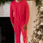 Male model standing in front of a white brick fireplace wearing the Men's Lounge Pants in Candy Cane and Men's Henley top in Cardinal