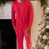 Male model standing in front of a white brick fireplace wearing the Men's Lounge Pants in Candy Cane and Men's Henley top in Cardinal