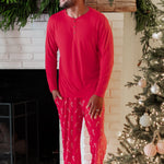 Male model walking looking off to the side in front of a white brick fireplace wearing the Men's Lounge Pants in Candy Cane and Cardinal men's Henley top