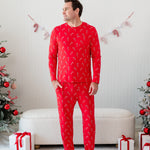 Male model standing with one hand in his pocket wearing the Men's Jogger Set in Candy Cane in front of a cream ottoman between two decorated Christmas trees