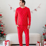 Male model standing with one hand in his pocket wearing the Men's Jogger Set in Candy Cane in front of a cream ottoman between two decorated Christmas trees