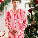 Modal wearing Men's Long Sleeve Pajama Set in red and white Peppermint Stripes print with Christmas tree in the background