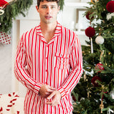 Modal wearing Men's Long Sleeve Pajama Set in red and white Peppermint Stripes print with Christmas tree in the background