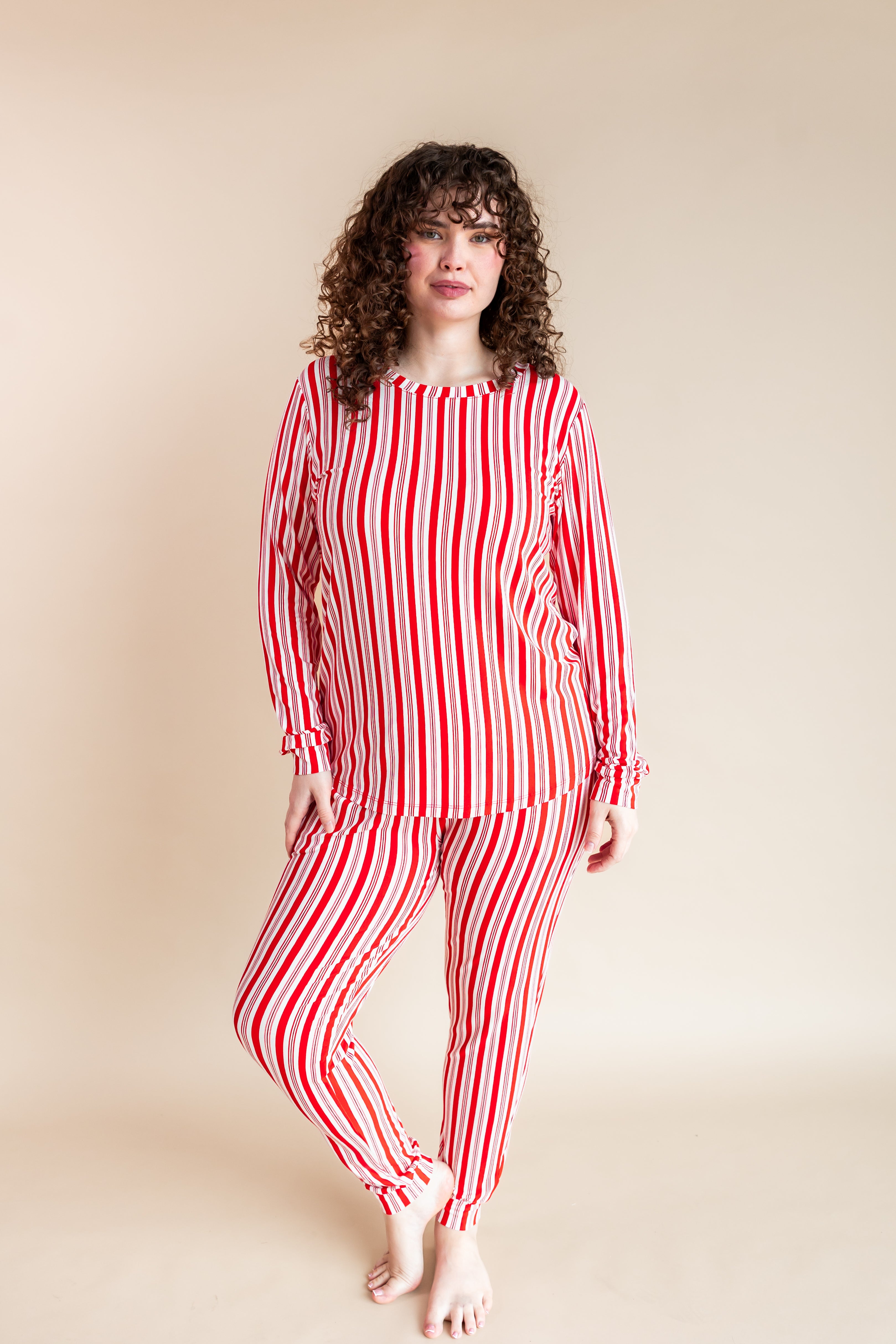 Woman wearing Women's Jogger Pajama Set in red and white Peppermint Stripes print on a beige background
