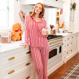 Modal posing in Long-Sleeved Women's Pajama Set in red and white Peppermint Stripes print standing in a kitchen holding a cup
