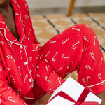 Close up of model sitting on the floor and holding a gift while wearing the Bamboo Long-Sleeved Women's Pajama Set in Candy Cane