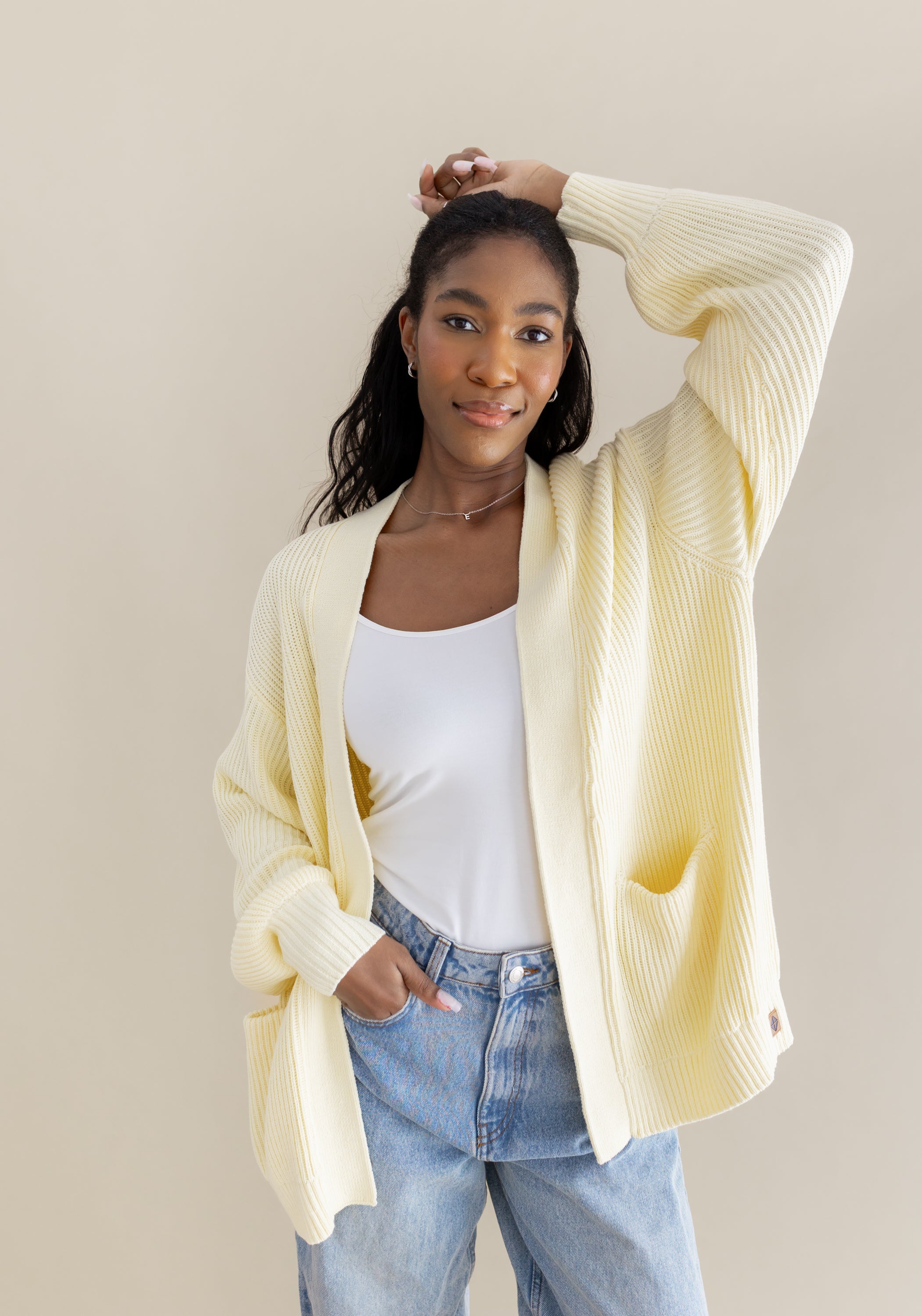 Female posing wearing the Chunky Knit Women's Oversized Cardigan in Chamomile with one hand in her jean pocket and one hand on herhead