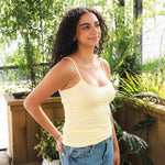 Woman wearing a yellow tank top and blue jeans standing in a garden setting.