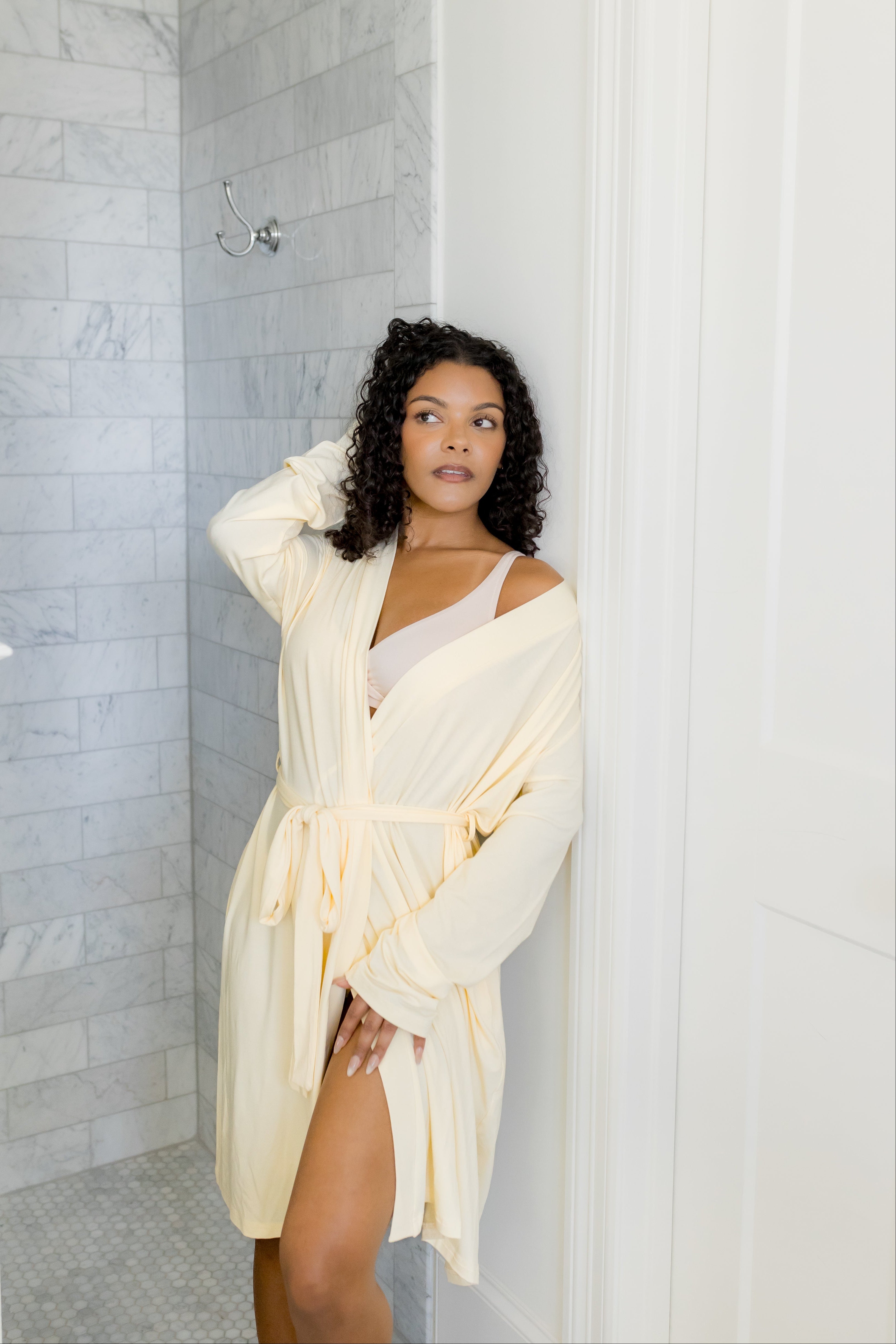 Woman in a yellow robe standing in a bathroom with marble tiles.