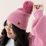 Focus is on the Pom on the hat and Kyte Baby's Leather Logo for the Chunky Knit Adult Pom Beanie in Apple Blossom 