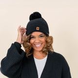 Model wearing  the Chunky Knit Adult Pom Beanie in Midnight with one hand on the brim of the beanie